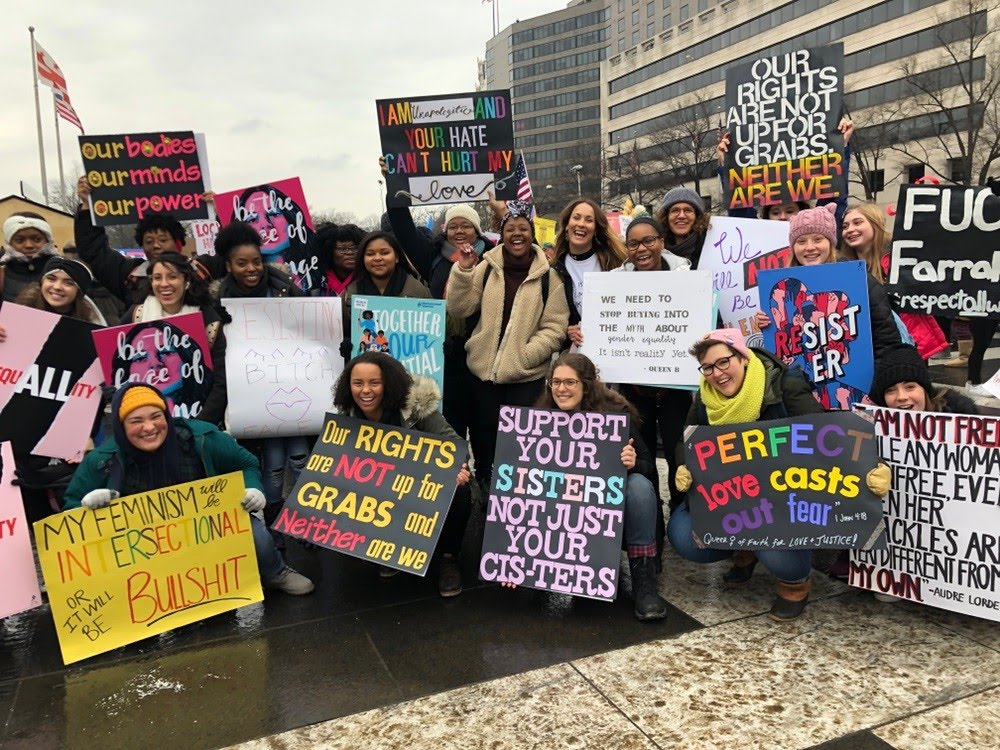 Students standing and kneeling, smiling, holding activist signs.