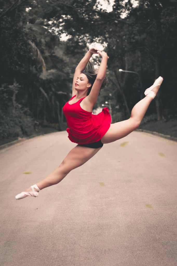 photo of ballerina split jumping in the middle of the road