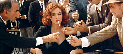 A woman having her cigarette lit by a bunch of men